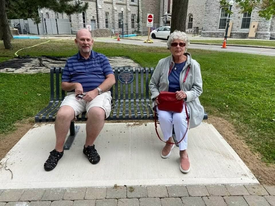 John-David Skene and his mother sitting together on a park bench outdoors.
